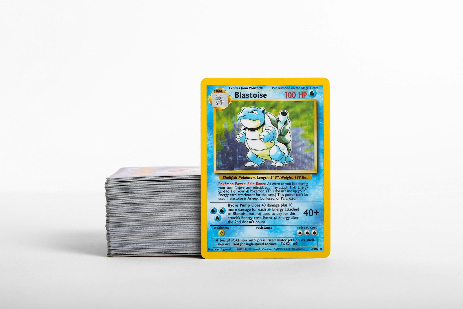 Una carta Pokémon di Blastoise accanto a una pila di carte collezionabili su una superficie chiara.