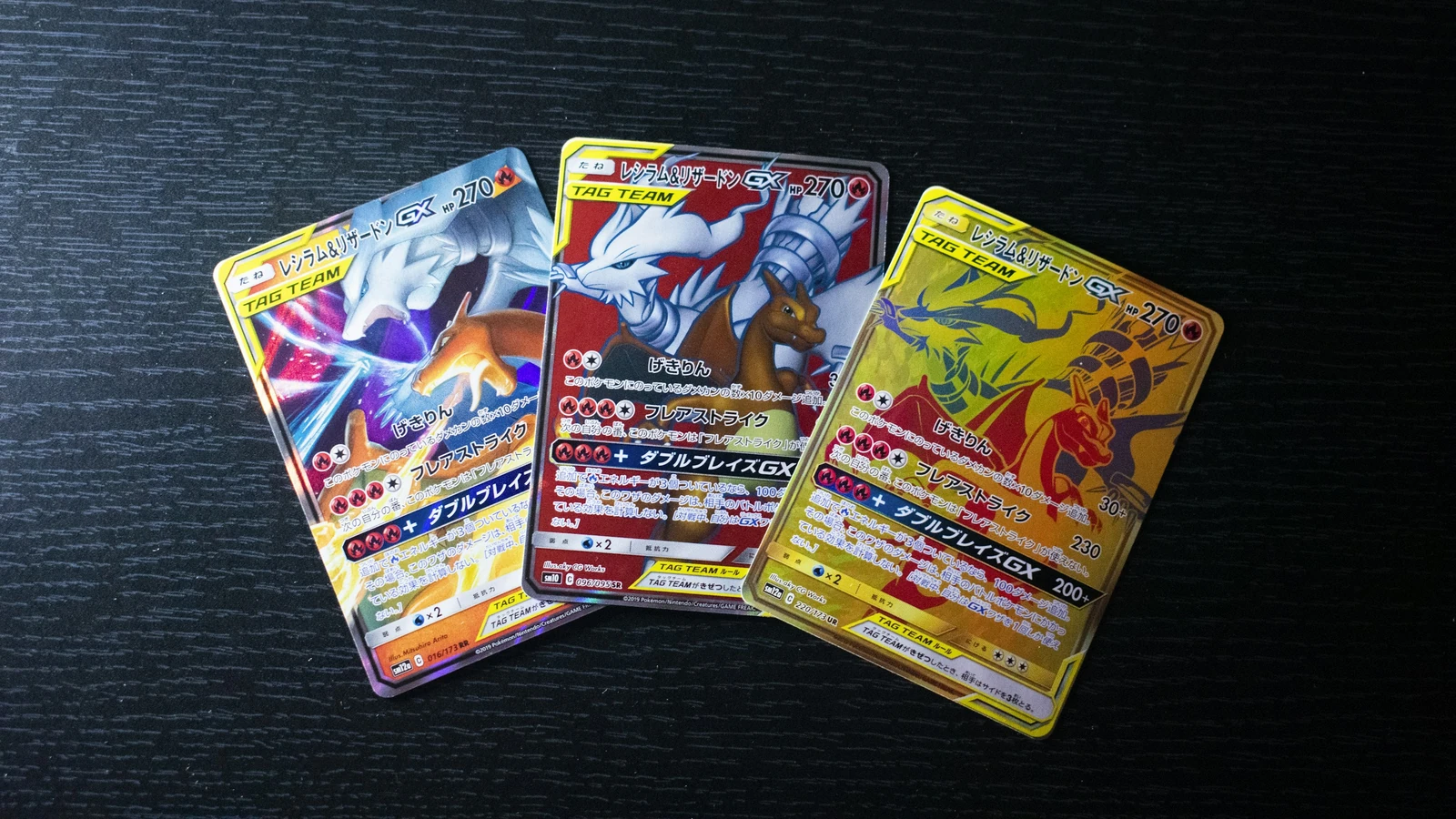 Tre carte Pokémon giapponesi con diverse versioni della stessa coppia di personaggi su un tavolo scuro